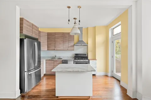 a kitchen with stainless steel appliances granite countertop a refrigerator a sink dishwasher a oven and a dining table with wooden floor