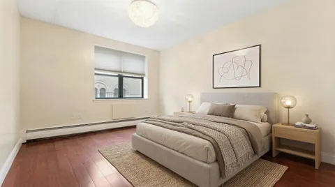 a bedroom with a bed and a lamp on dresser with wooden floor