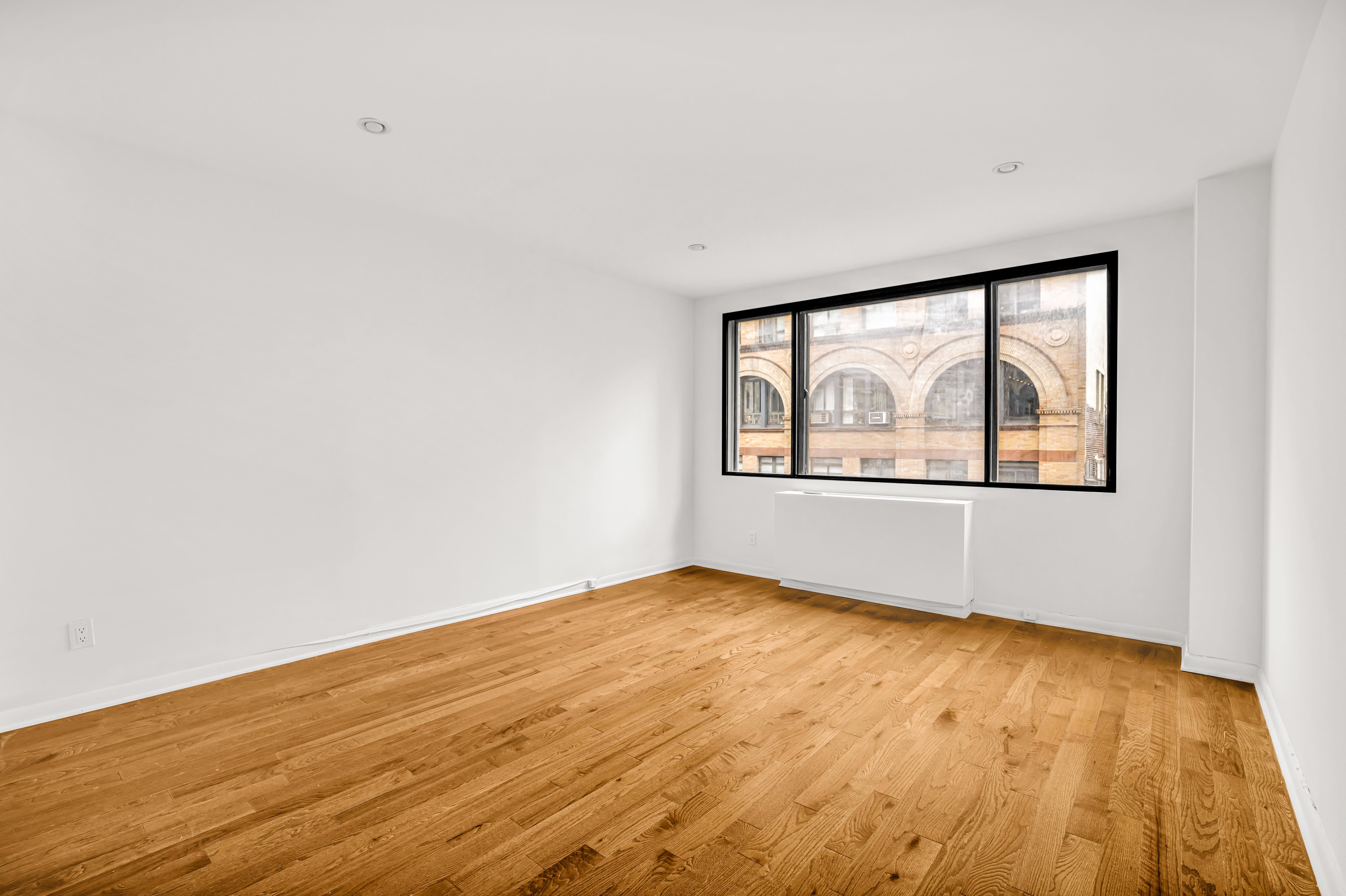 44 East 12th Street, Unit 8E Manhattan, NY 10003 - Photo 3 of 7 an empty room with wooden floor and windows