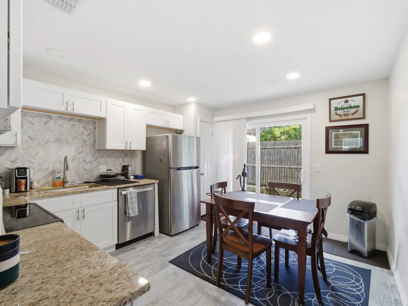 a kitchen with stainless steel appliances kitchen island granite countertop a dining table chairs and a refrigerator