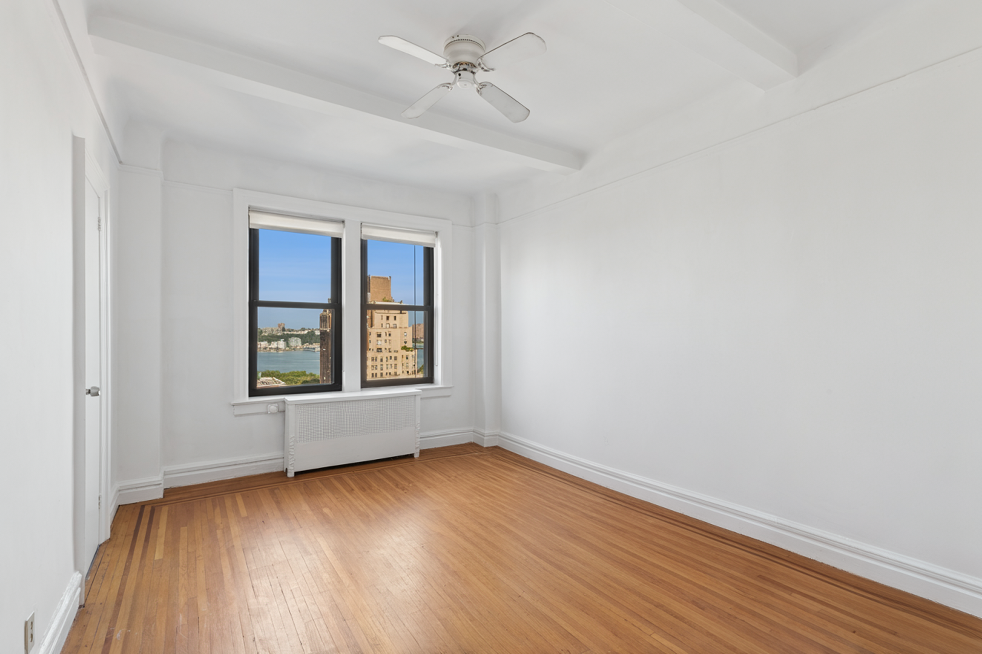 710 West End Avenue, Unit 14B Manhattan, NY 10025 - Photo 14 of 19 an empty room with wooden floor chandelier fan and windows