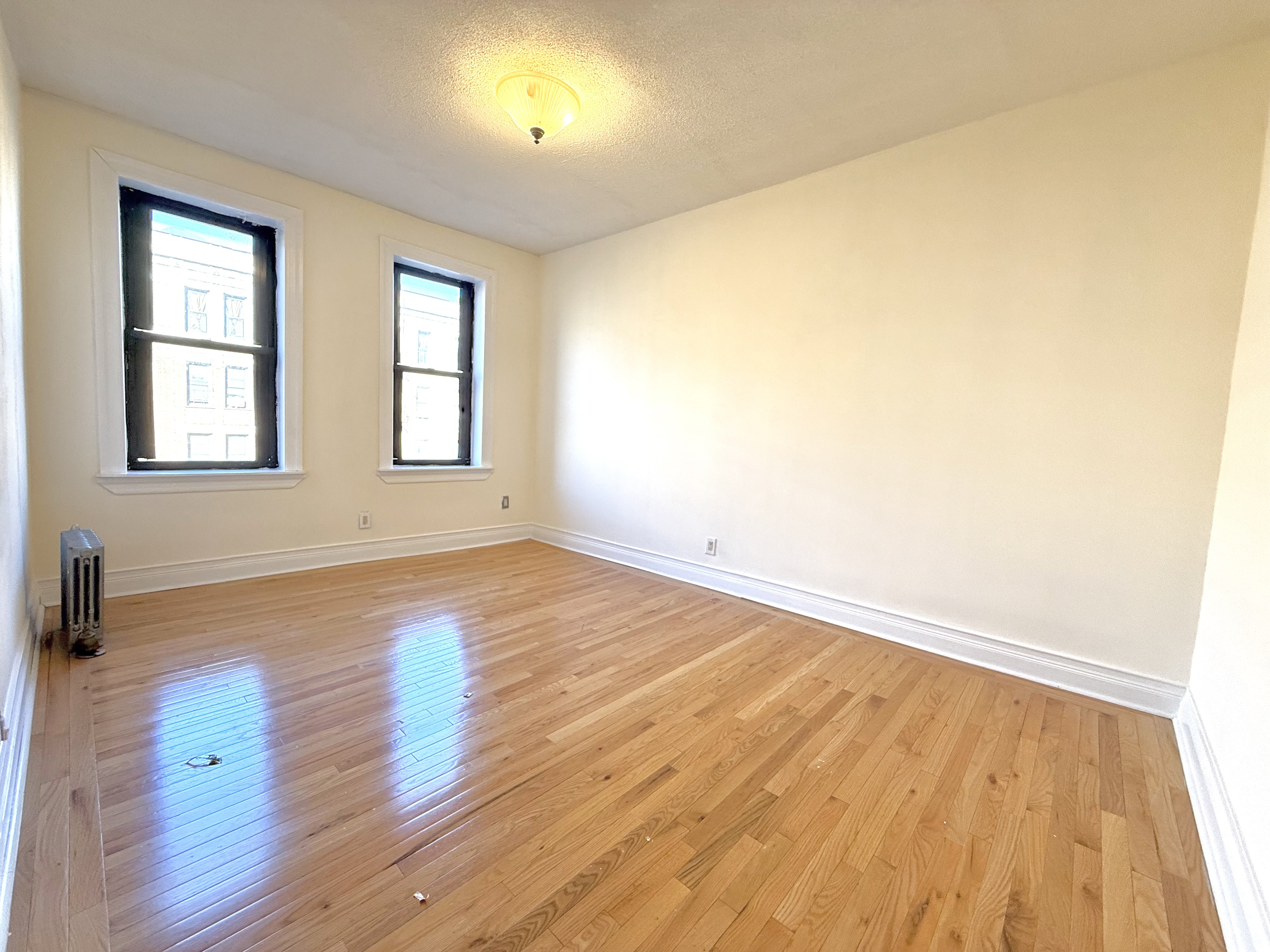 133 Seaman Avenue, Unit 3A Manhattan, NY 10034 - Photo 4 of 7 an empty room with wooden floor and windows