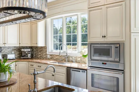 a kitchen with kitchen island granite countertop a sink cabinets stainless steel appliances and a chandelier