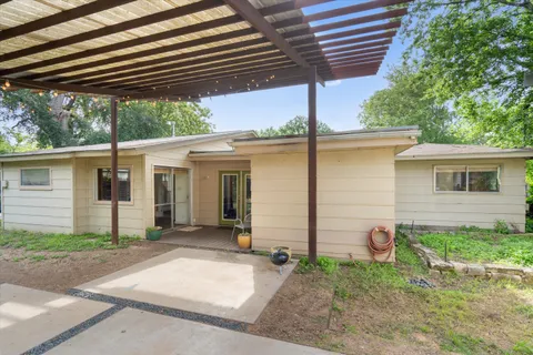 a backyard of house with table and chairs under an umbrella with a large tree