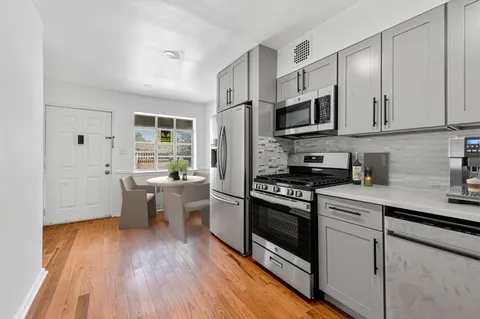 a kitchen with stainless steel appliances a stove top oven a sink a refrigerator white cabinets and wooden floor