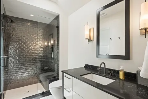 a bathroom with a granite countertop sink a toilet a mirror and shower