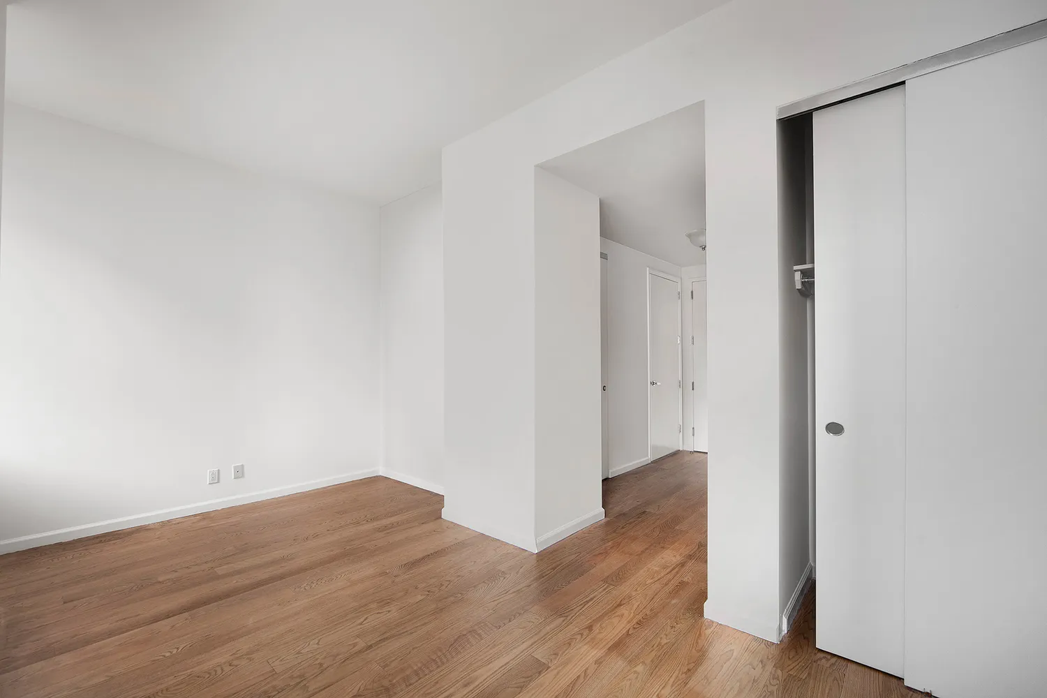 a view of an empty room with wooden floor and closet