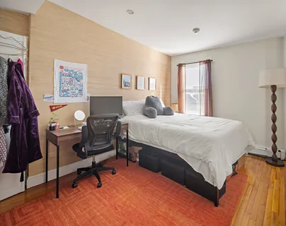 a bedroom with a bed a desk and chair with the wooden floor
