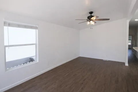 an empty room with wooden floor fan and windows