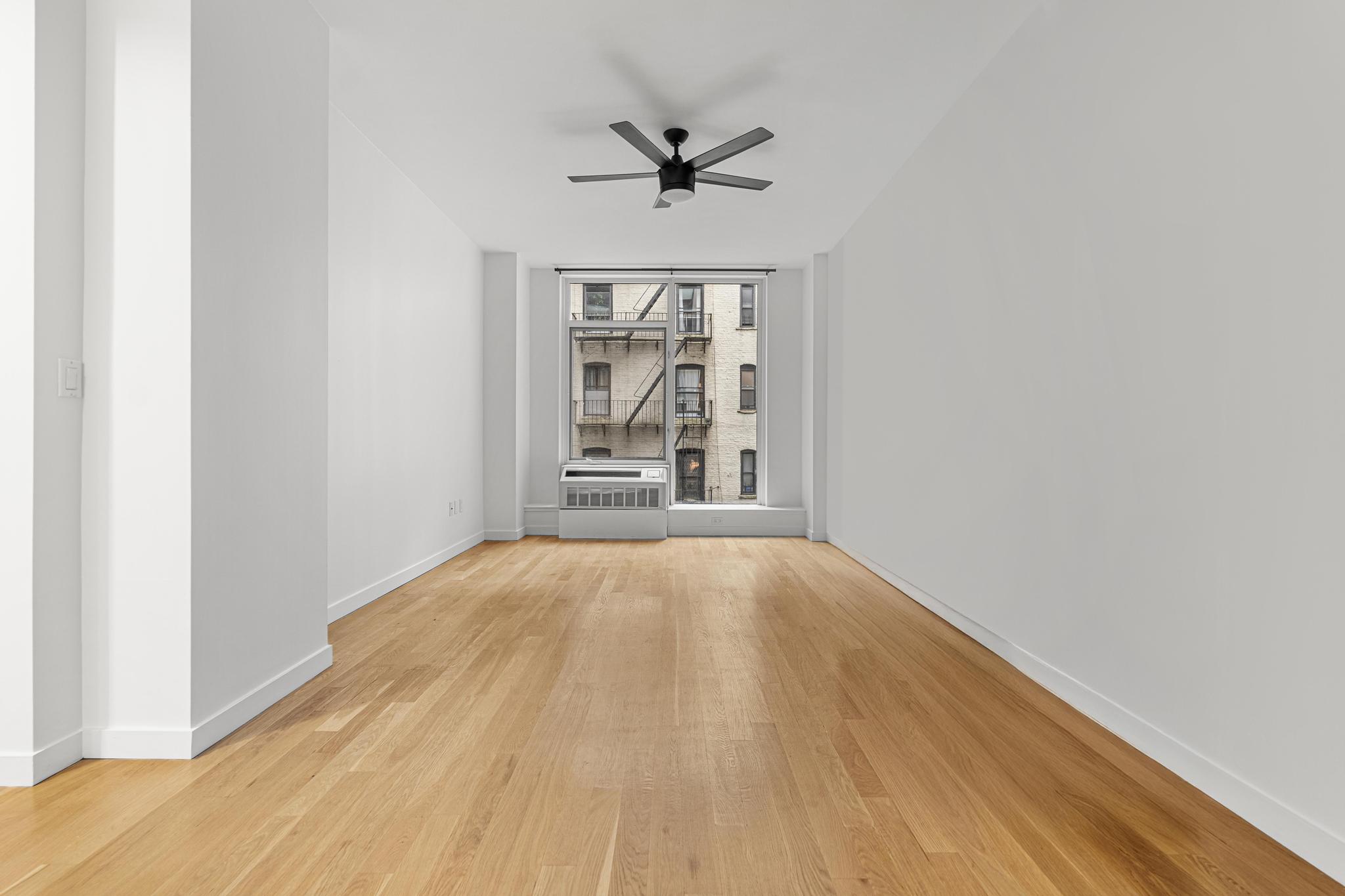 306 West 116th Street, Unit 1C Manhattan, NY 10026 - Photo 6 of 12 an empty room with wooden floor a ceiling fan and windows
