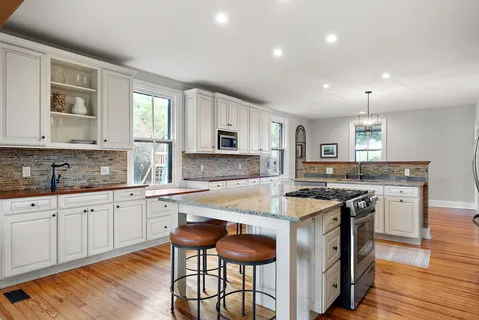a kitchen with stainless steel appliances granite countertop a stove top oven a sink dishwasher and white cabinets with wooden floor