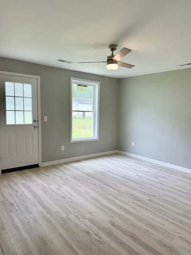 an empty room with wooden floor chandelier fan and windows