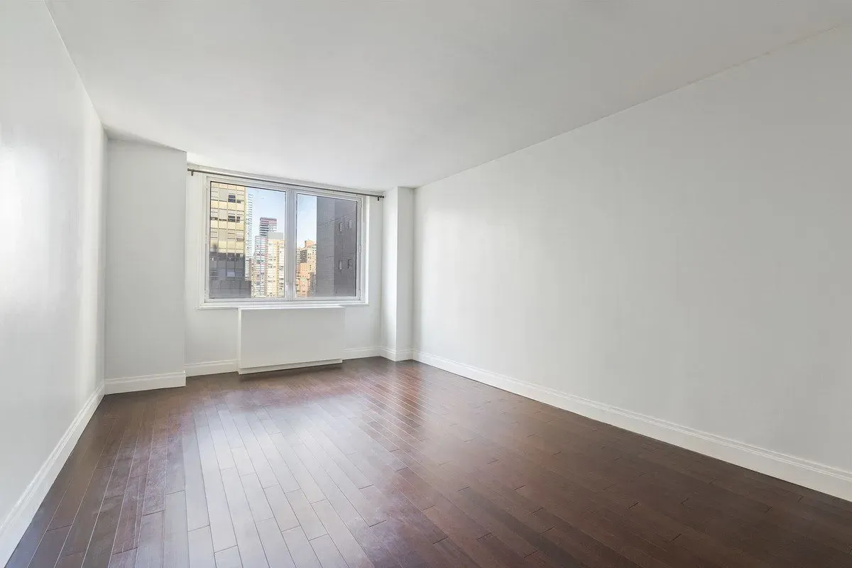 212 East 47th Street, Unit 21D Manhattan, NY 10017 - Photo 4 of 16 an empty room with wooden floor and windows