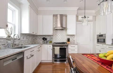 a kitchen with stainless steel appliances a stove a sink dishwasher a refrigerator white cabinets and wooden floor next to a window