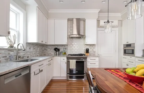 a kitchen with stainless steel appliances a stove a sink dishwasher a refrigerator white cabinets and wooden floor next to a window