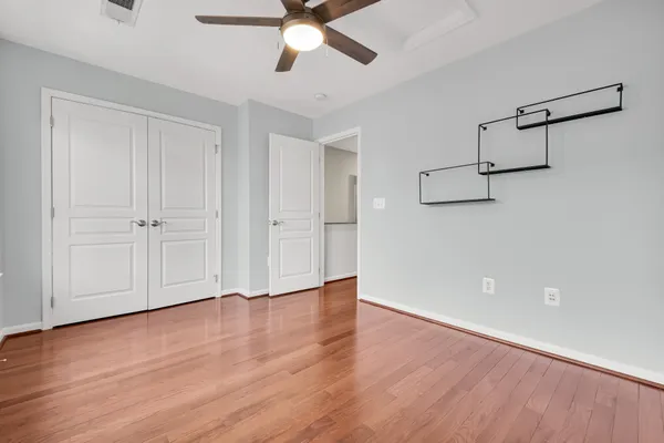 an empty room with wooden floor closet fan and windows