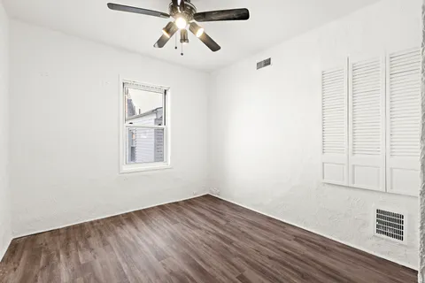 an empty room with wooden floor fan and windows
