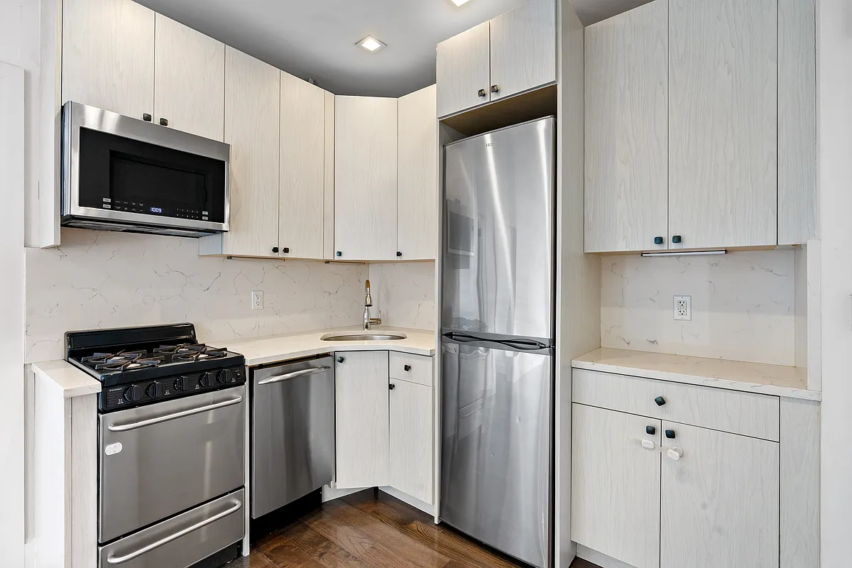 152 Thompson Street, Unit 2B Manhattan, NY 10012 - Photo 7 of 10 a kitchen with stainless steel appliances white cabinets and a stove a refrigerator with wooden floor