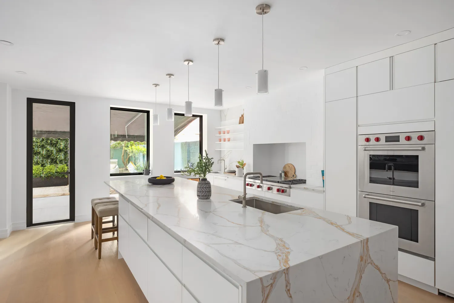 a kitchen with stainless steel appliances a stove a sink a microwave a refrigerator and white cabinets with wooden floor