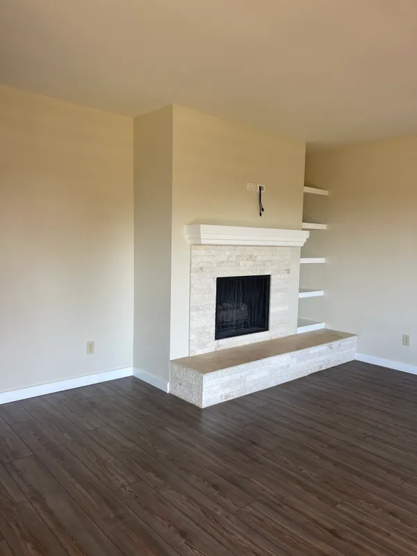 a view of an empty room with wooden floor and a fireplace