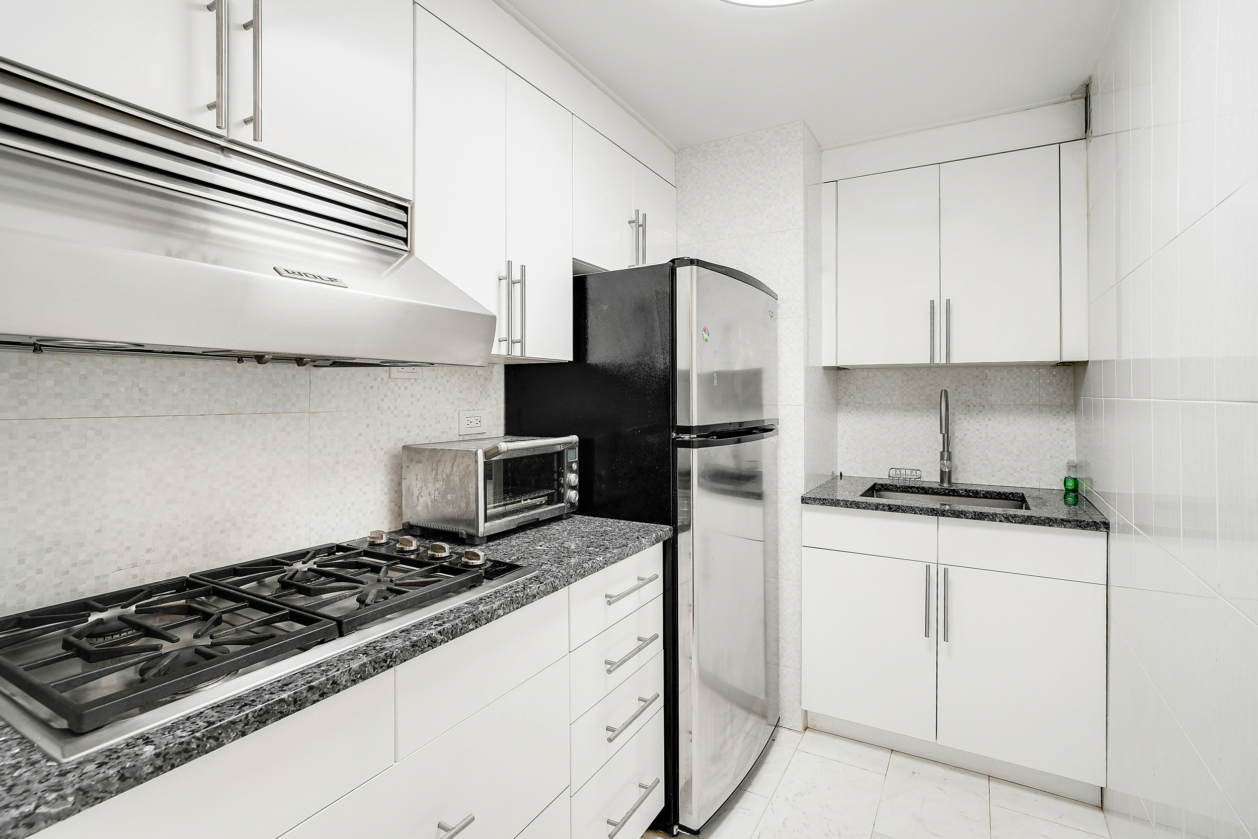 135 East 54th Street, Unit 12M Manhattan, NY 10022 - Photo 3 of 10 a kitchen with granite countertop a stove sink and refrigerator