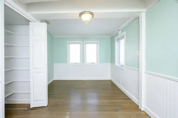 a view of an empty room with wooden floor and window