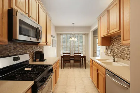 a kitchen with stainless steel appliances granite countertop a stove top oven a sink a dining table and chairs with wooden floor