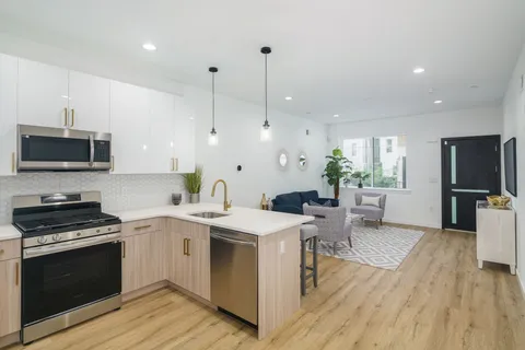 a kitchen with stainless steel appliances a stove a sink dishwasher a refrigerator white cabinets and wooden floor