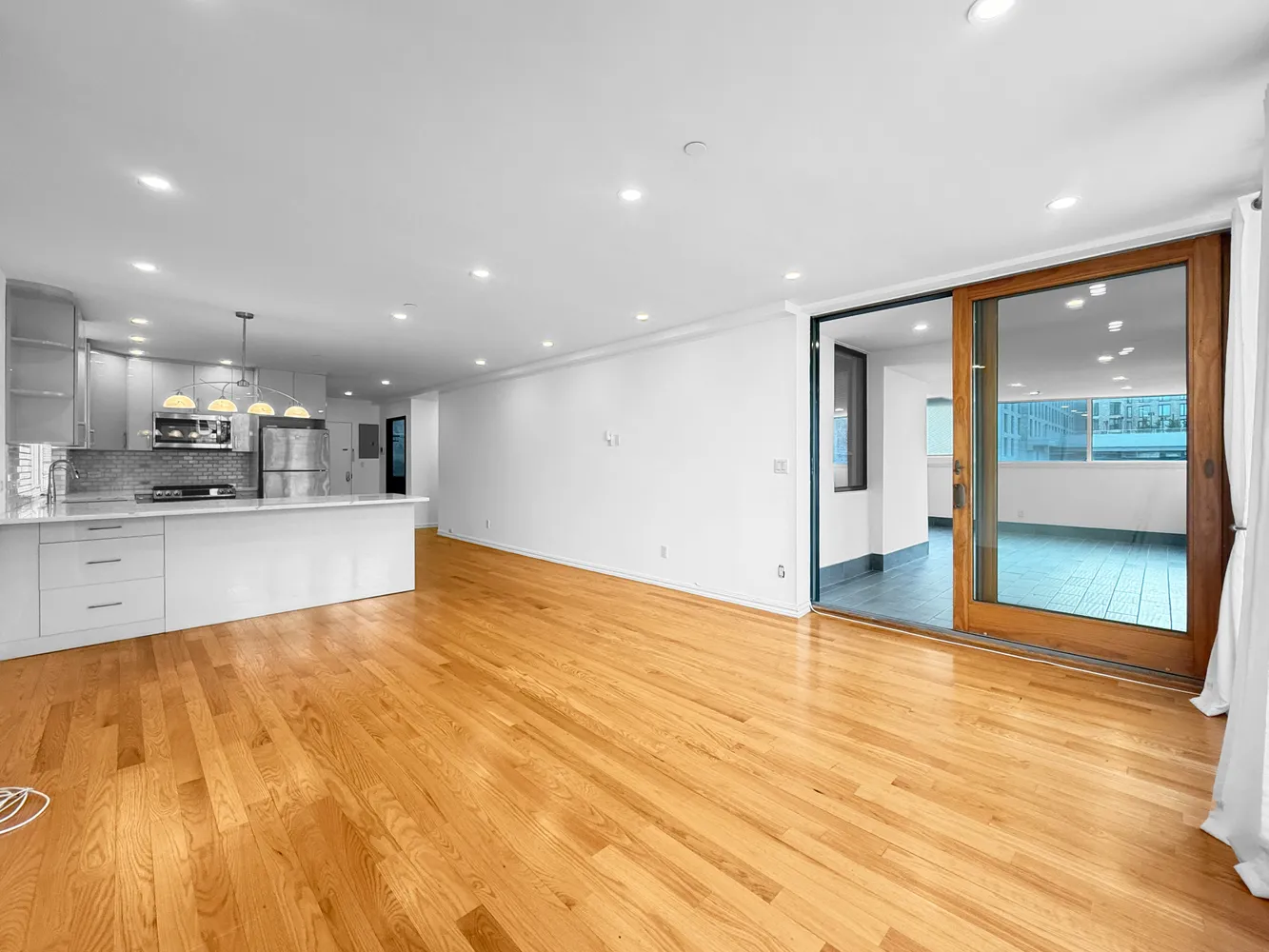 a view of an empty room with kitchen counter space and wooden floor
