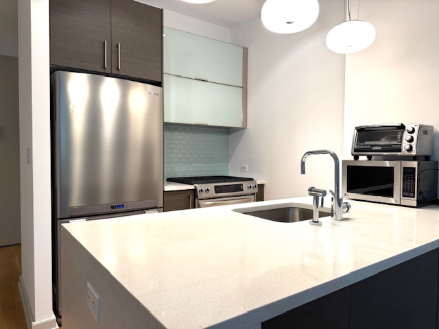 21-45 44th Drive, Unit 1H Queens, NY 11101 - Photo 2 of 7 a kitchen with stainless steel appliances a sink a stove and a refrigerator with wooden floor