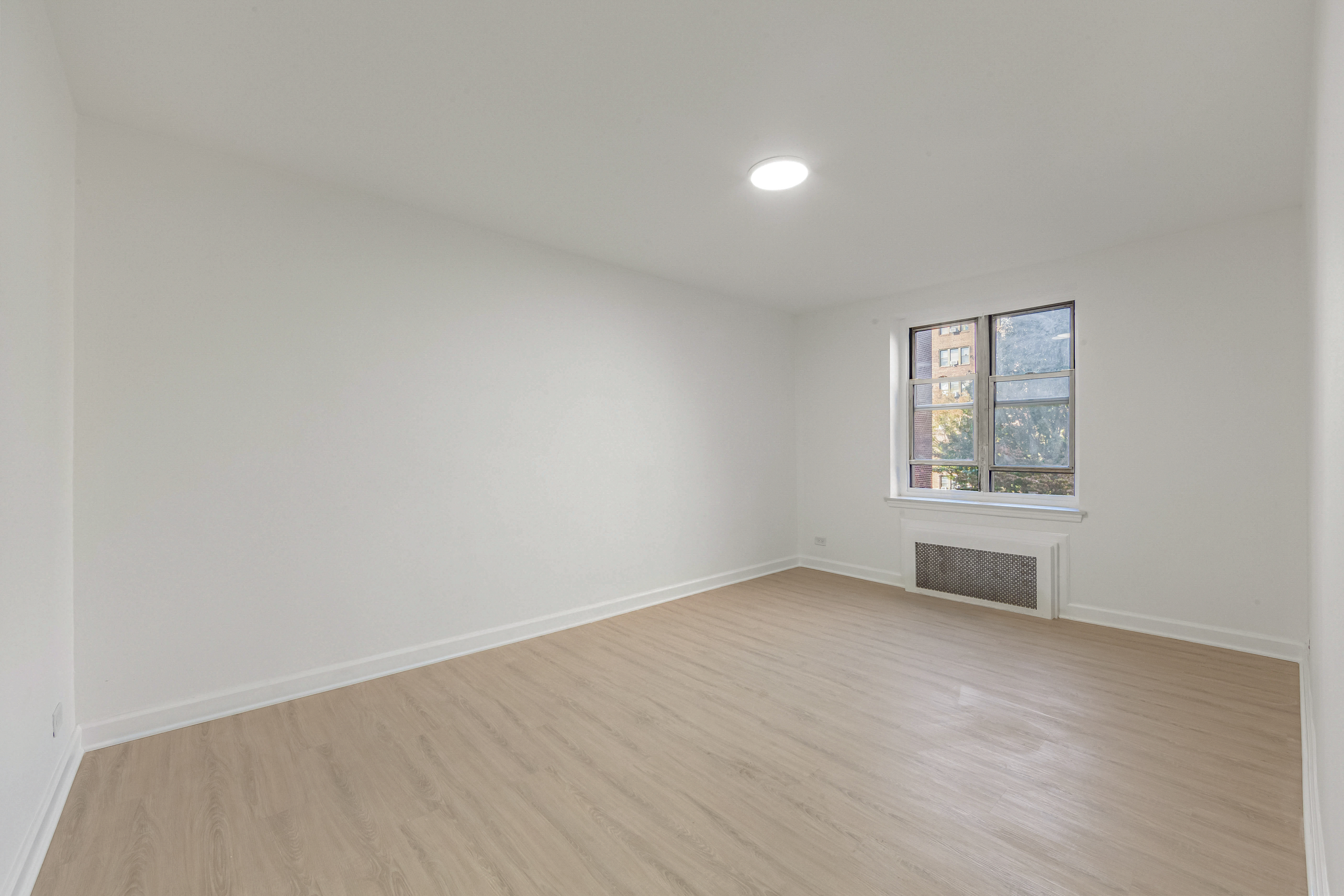 76-10 34th Avenue, Unit 2H Queens, NY 11372 - Photo 4 of 12 an empty room with wooden floor and windows