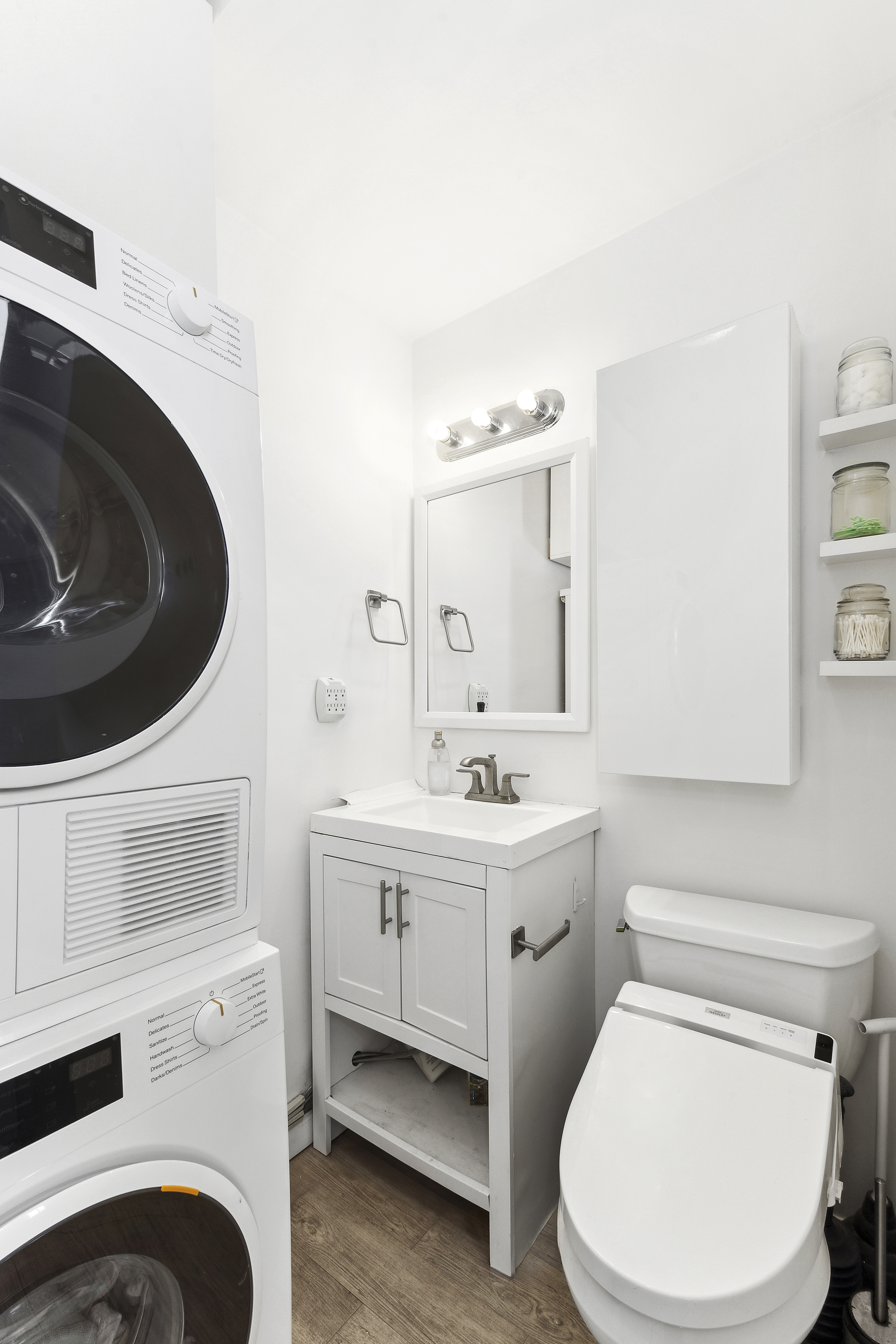 124 Thompson Street, Unit 21 Manhattan, NY 10012 - Photo 4 of 11 a bathroom with a toilet sink washing machine and mirror