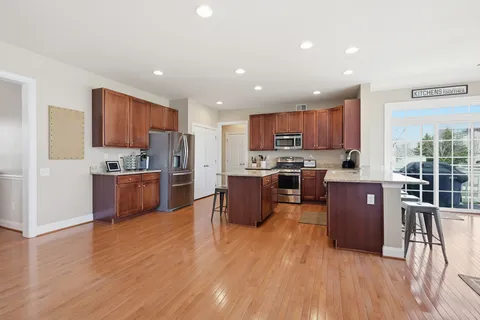 a kitchen with stainless steel appliances wooden floors wooden cabinets a stove a sink and a window