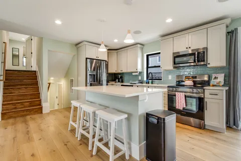 a kitchen with kitchen island granite countertop a stove top oven a sink a refrigerator white cabinets and wooden floor