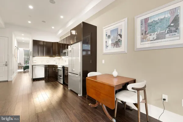 a kitchen with stainless steel appliances kitchen island granite countertop a refrigerator a stove a sink a dining table and chairs with wooden floor