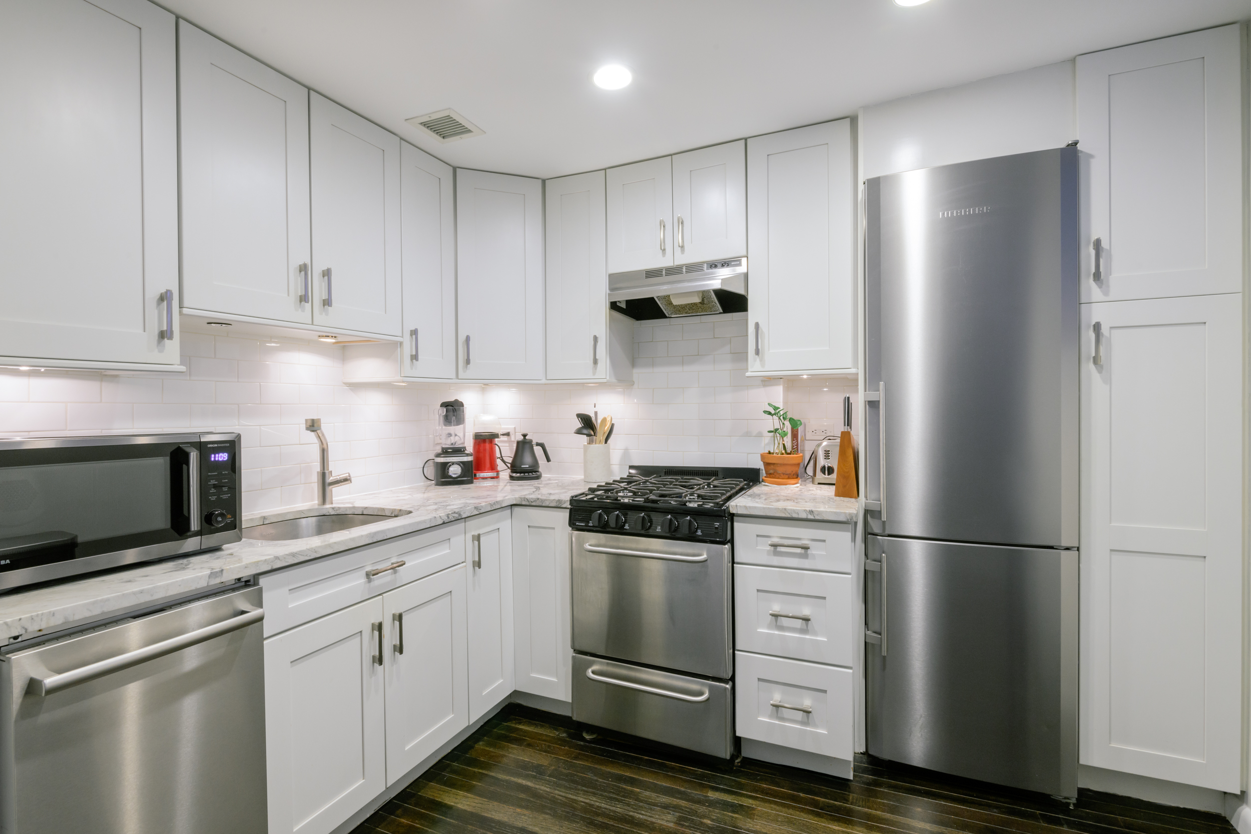 211 Thompson Street, Unit 4J Manhattan, NY 10012 - Photo 3 of 8 a kitchen with white cabinets and stainless steel appliances