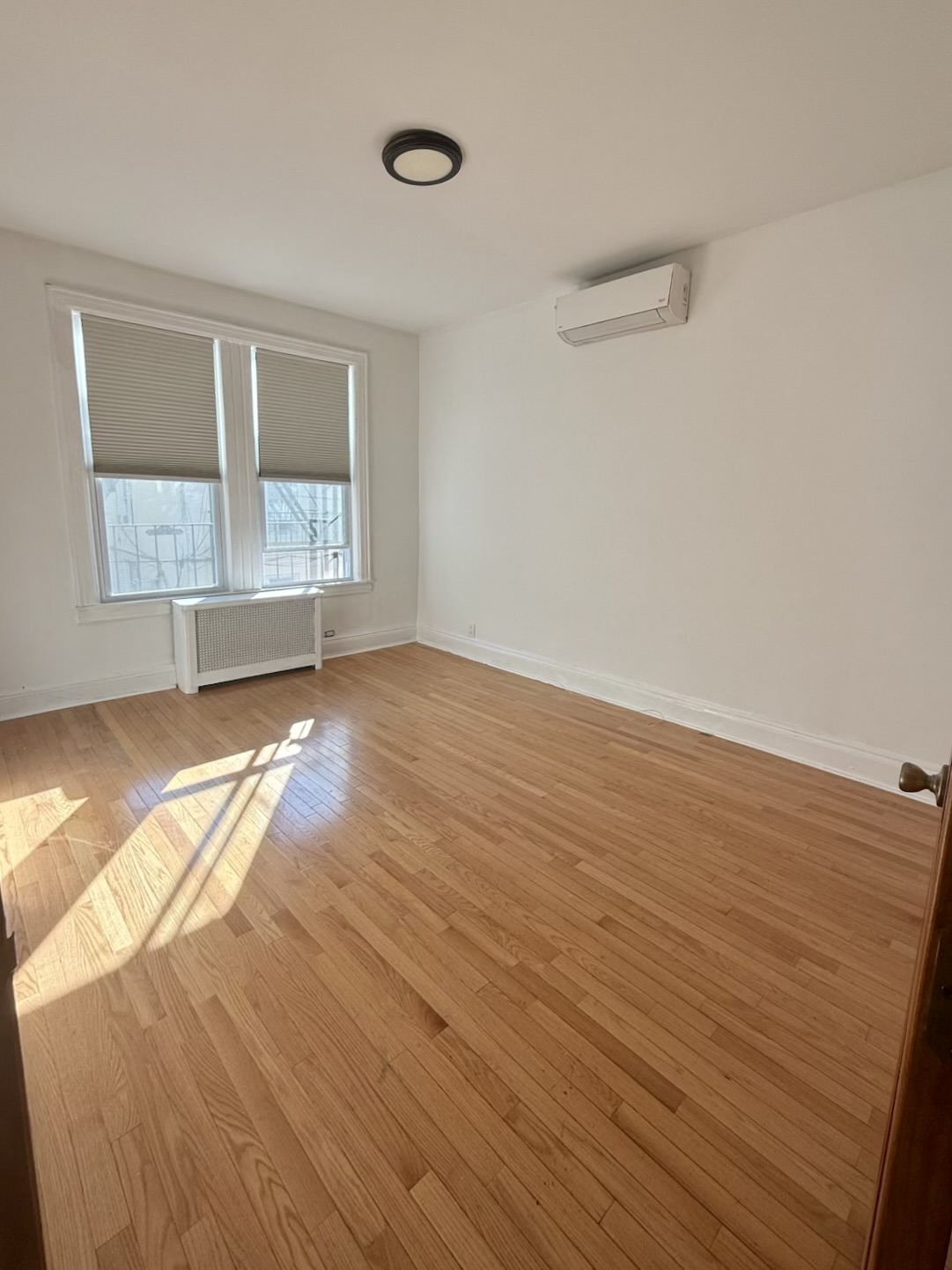18-48 21st Drive, Unit 1R Queens, NY 11105 - Photo 5 of 11 an empty room with wooden floor and windows