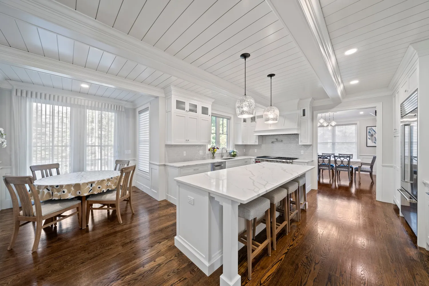 a large kitchen with kitchen island a stove a sink a refrigerator and white cabinets with wooden floor