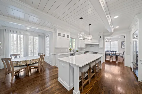 a large kitchen with kitchen island a stove a sink a refrigerator and white cabinets with wooden floor