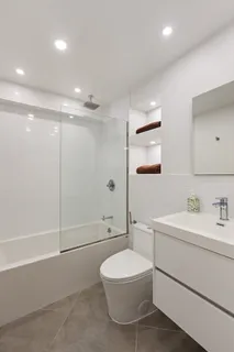 a bathroom with a toilet a sink a mirror a shower a vanity and window