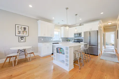 a kitchen with a dining table chairs wooden floor cabinets and appliances