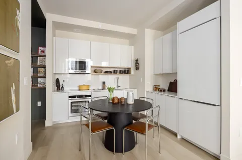 a living room with stainless steel appliances a dining table wooden floor and a refrigerator