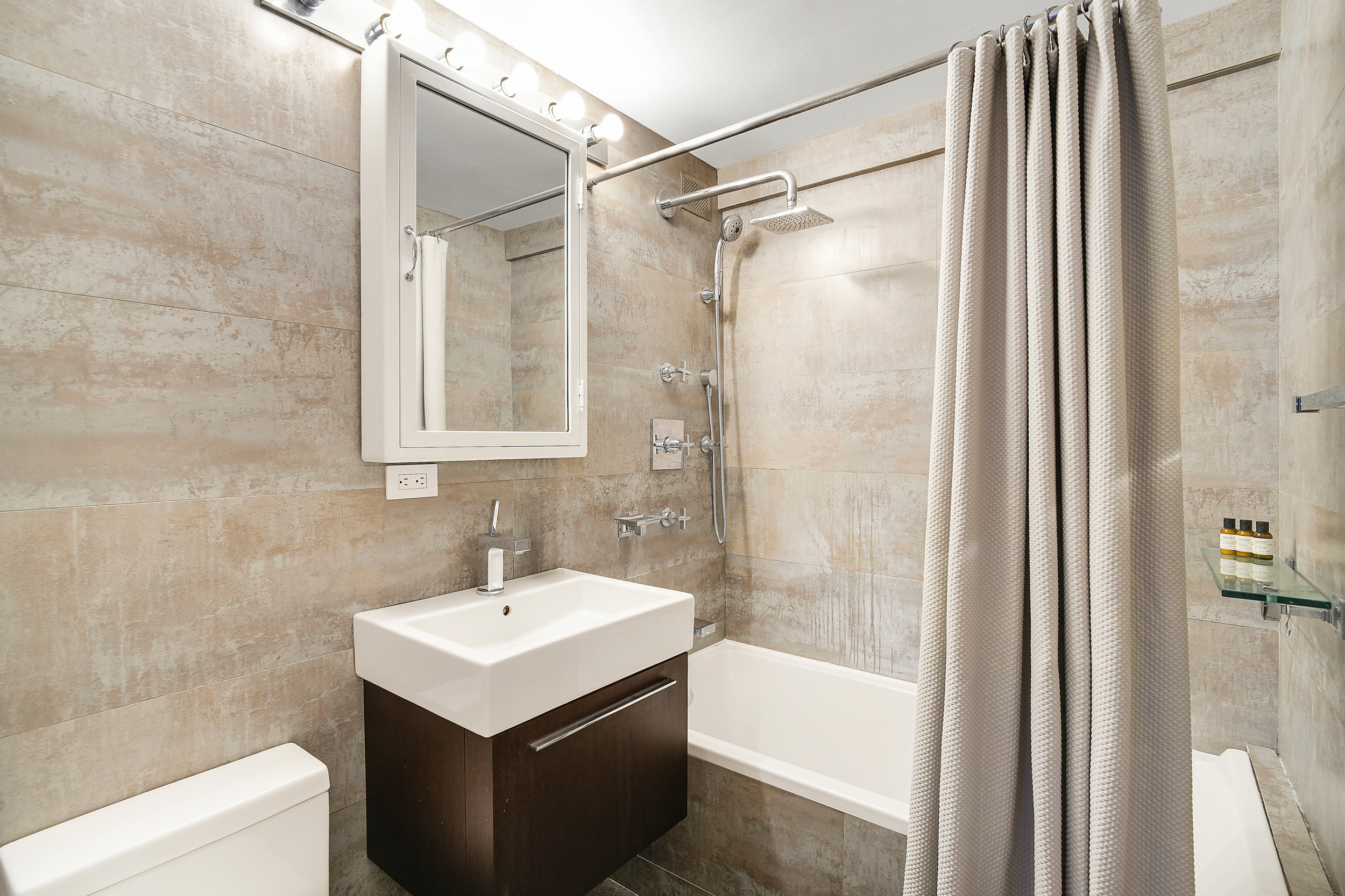 135 East 54th Street, Unit 12M Manhattan, NY 10022 - Photo 7 of 10 a bathroom with a sink a mirror and a shower
