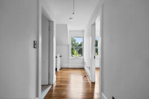 a view of a hallway with wooden floor and a bathroom