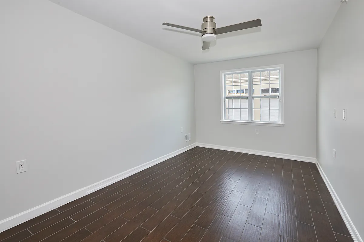 10220 Rockaway Beach Boulevard, Unit 1A Queens, NY 11694 - Photo 4 of 8 an empty room with wooden floor ceiling fan and windows