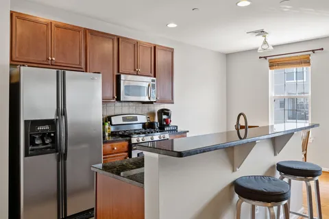 a kitchen with stainless steel appliances granite countertop a refrigerator a sink a stove and chairs