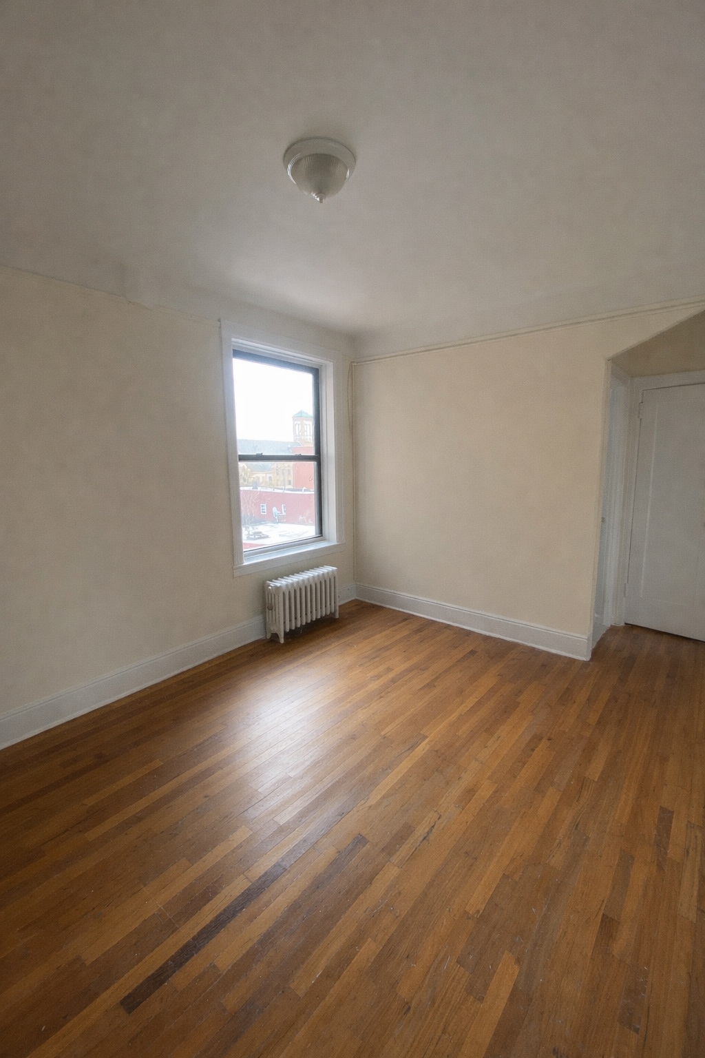 28-23 42nd Street, Unit D5 Queens, NY 11103 - Photo 4 of 10 an empty room with wooden floor and windows