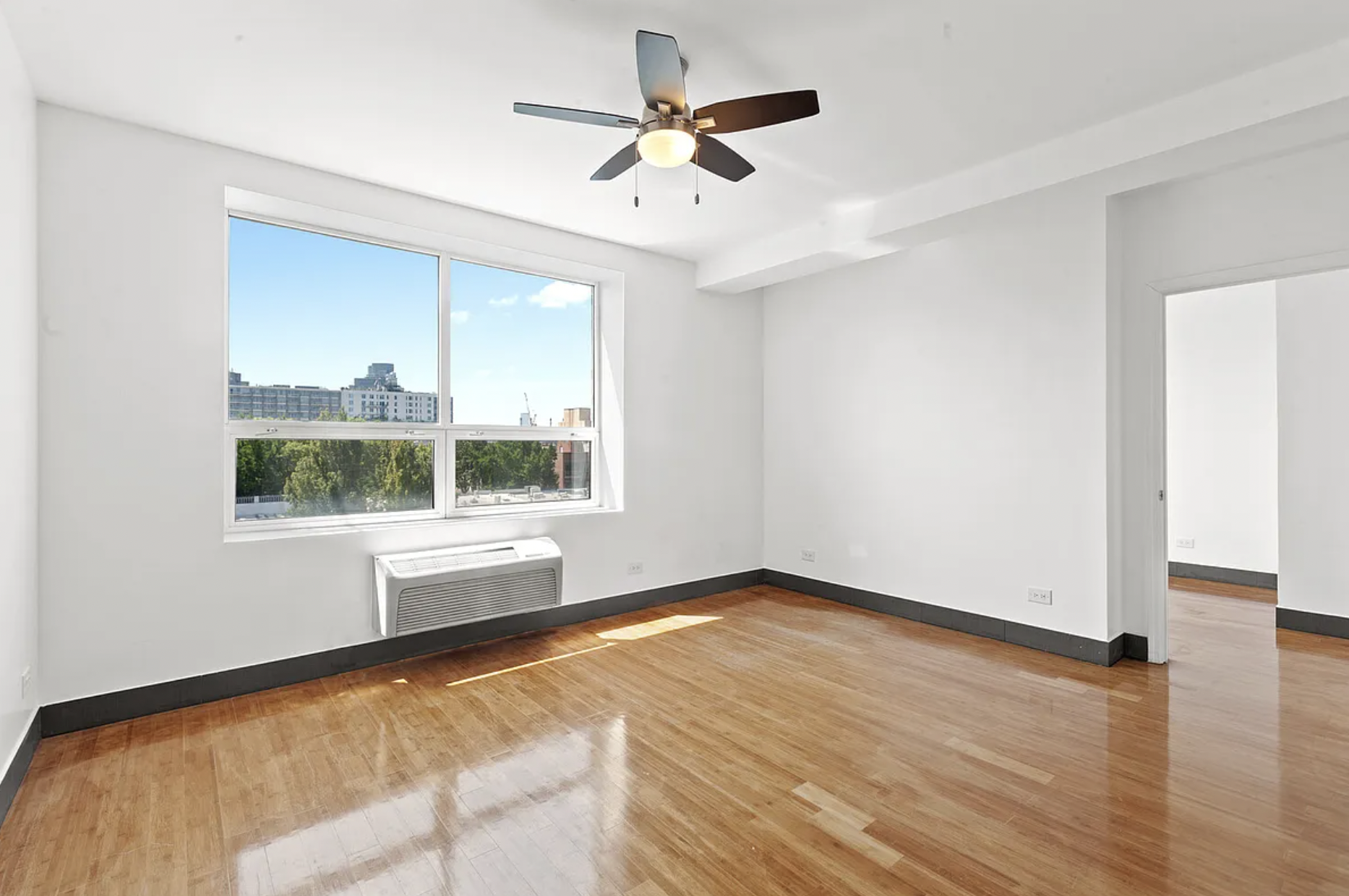 a view of an empty room with a window and wooden floor