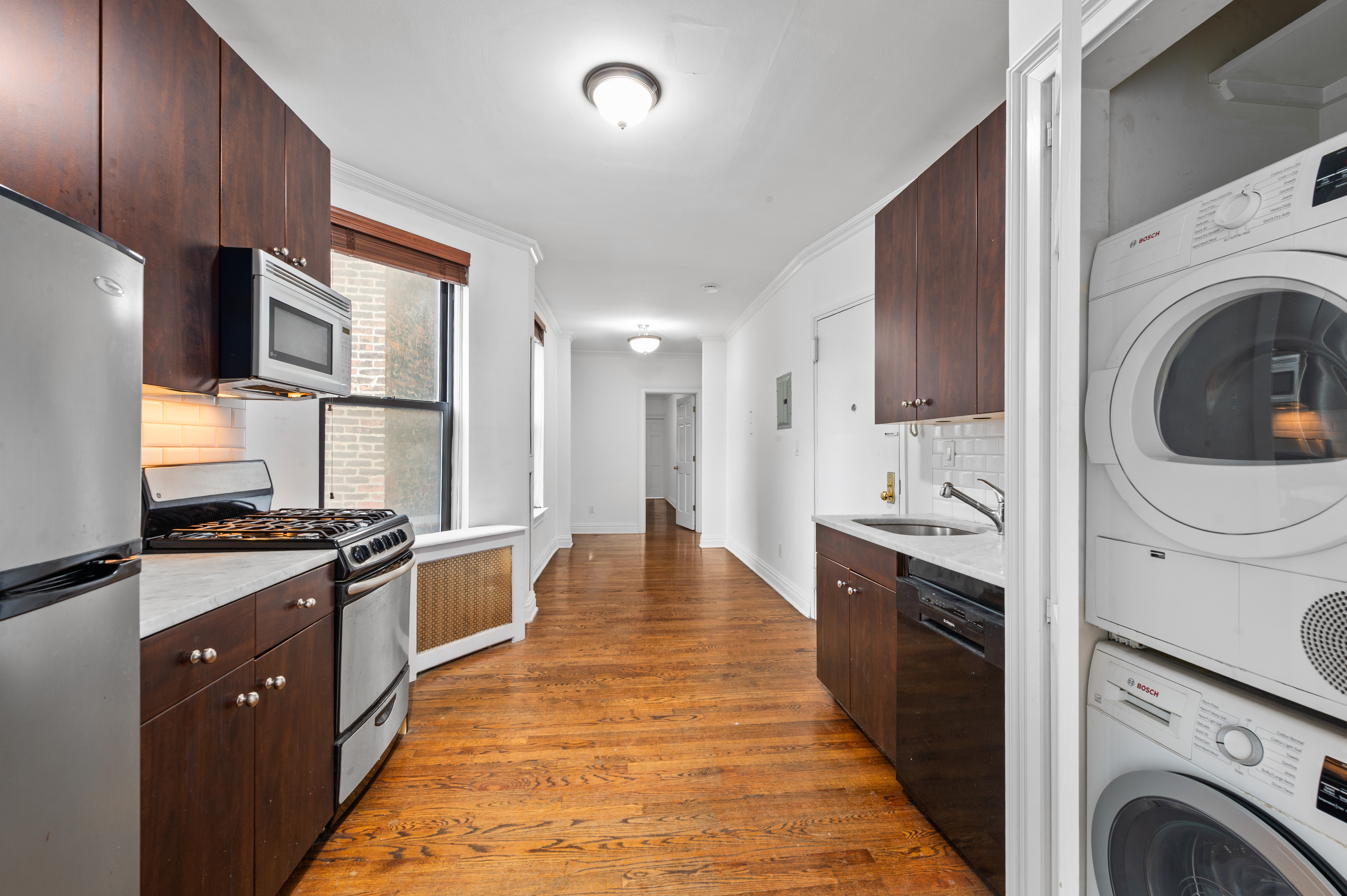 142 Sullivan Street, Unit 21 Manhattan, NY 10012 - Photo 3 of 8 a kitchen with stainless steel appliances granite countertop a stove top oven a sink dishwasher and a refrigerator with wooden cabinets
