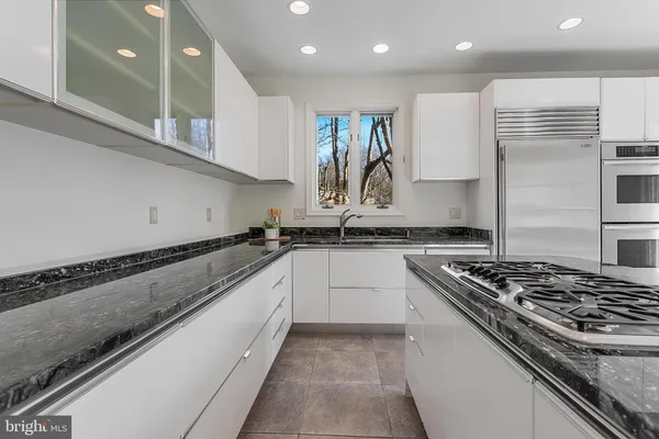 a kitchen with granite countertop a stove a sink a refrigerator and blue cabinets with wooden floor
